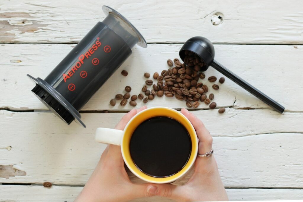 a person holding a cup of coffee next to a pile of coffee beans